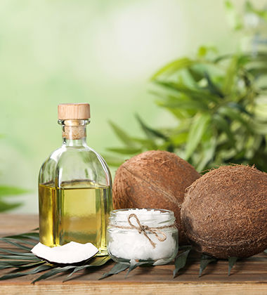 coconut oil in a glass bottle placed next to raw and shredded coconuts