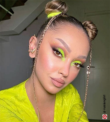 woman sitting with space buns and neon eyeshadow on the inner corner